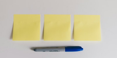 Three yellow sticky Post-it notes on a white bakcground with a blue Sharpie marker pen beneath them