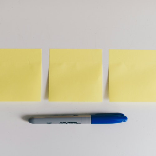 Three yellow sticky Post-it notes on a white bakcground with a blue Sharpie marker pen beneath them