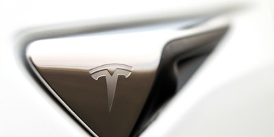 A white Tesla logo on a silver-coloured handle against a white background