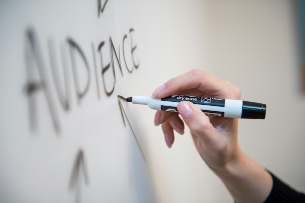 A hand holds a black marker pen over a whiteboard on which the word 'audience' is written with arrows pointing towards it
