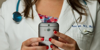 A doctor wearing a stethoscope uses a handheld device