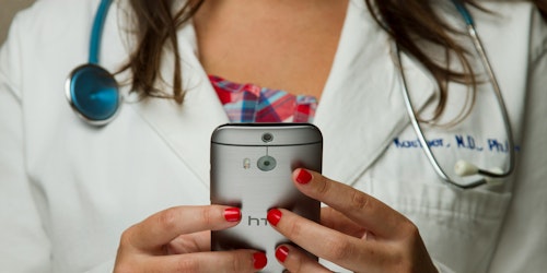 A doctor wearing a stethoscope uses a handheld device