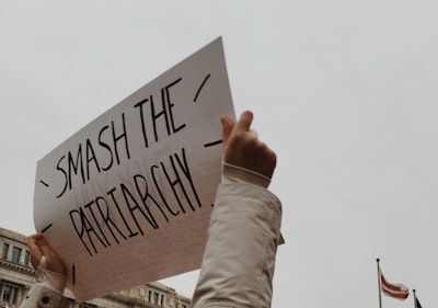 Two hands hold up a sign that reads 'smash the patriarchy' 