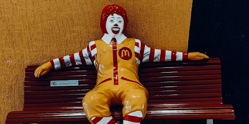 A statue of Ronald McDonald sitting on a bench