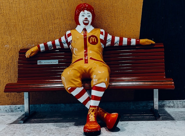 A statue of Ronald McDonald sitting on a bench