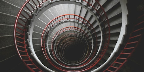 A photo taken down the middle of a concrete spiral staircase with a red handrail