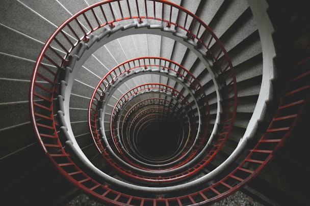 A photo taken down the middle of a concrete spiral staircase with a red handrail