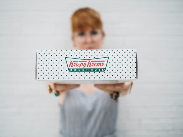 Person presenting a box of Krispy Kreme doughnuts