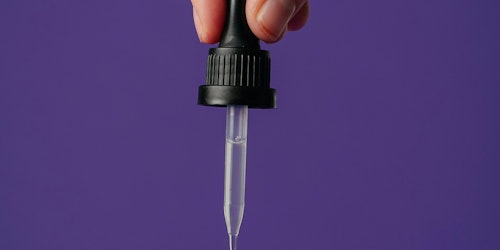 A hand squeezes a drop of liquid from a pipette 