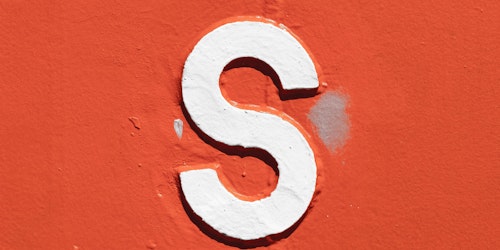 A white letter 's' with a black outline painted onto an orange wall
