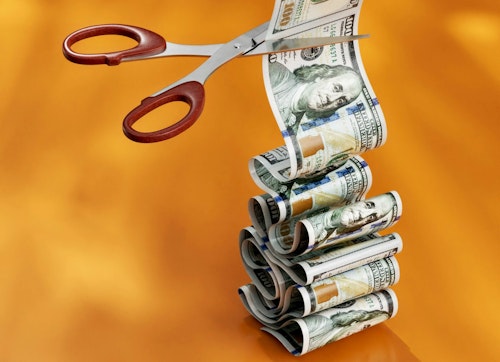 A pair of scissors positioned to cut across a reem of hundred dollar bills is 