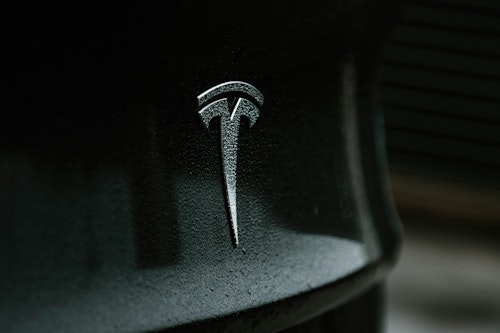 A rain-flecked Tesla badge on a grey car
