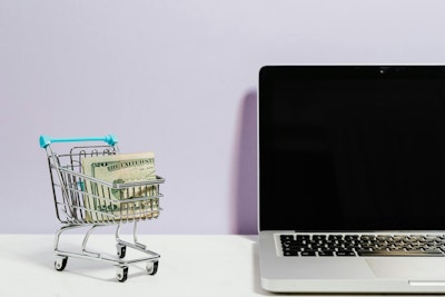 A shopping trolley containing bank notes next to a laptop, representing omnichannel customer service in the retail sector