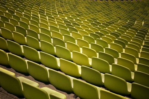 The backs of green empty rows of chairs at a stadium