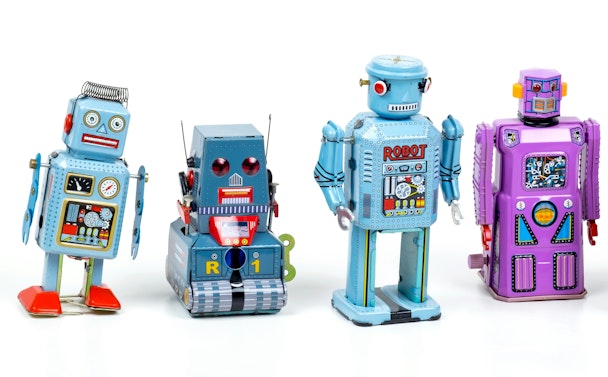 Four tin toy robots in a line against a white background