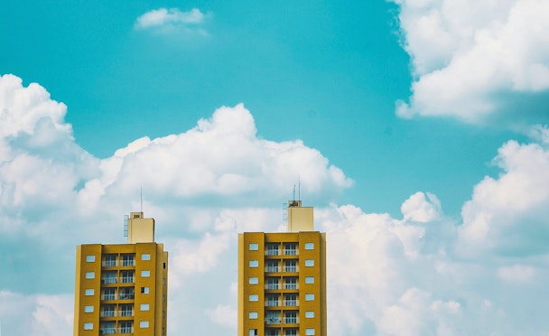 The tops of two yellow tower blocks stand before clouds in a blue sky