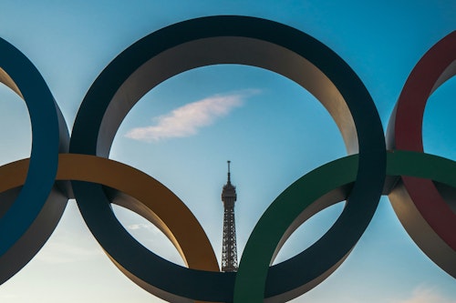 The Eiffel Tower is visible through one of the Olympic rings