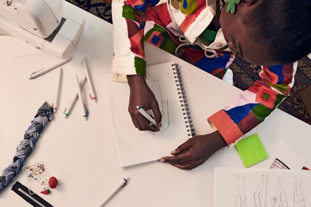 Woman using Uniball pens to sketch a fashion design on a table