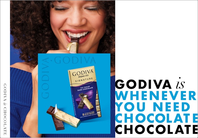 Girl with afro biting into a small Godiva chocolate bar and smiling