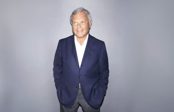 Sir Martin Sorrell, wearing a navy blue blazer with gray trousers and a white shirt open at the neck 