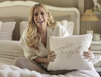 Reality TV star Stacey Solomon sits on a bed holding a pillow that reads 'let's snuggle'