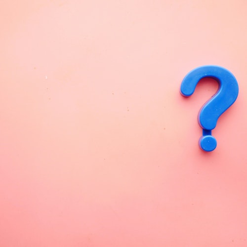 A blue plastic question mark against a pink background