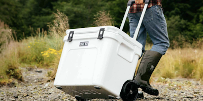 A Yeti cooler being wheeled over rough terrain by a person wearing rubber boots