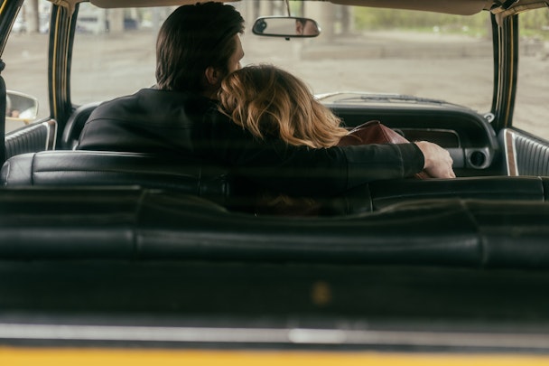 In a car, a man puts his arm round a woman in the old money aesthetic