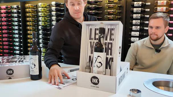 n-fuzers Simon Rayfield and Jack Beaumont at House of Accolade with the KRINK x Barossa Ink by Grant Burge wines box, wine bottle, ink and pen, flyer and serial numbered card. The box is transformed into its upright position with the bottle on show. Behind the scene is racking filled with hundreds of wine bottles.