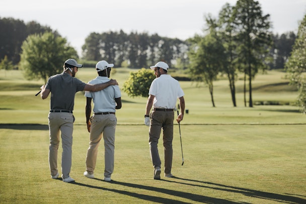 Three male golfers walk on a golf pitch in the old money aesthetic